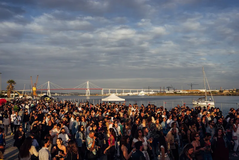 Wide view of the crowd gathered by the waterfront with the bridge in the distance